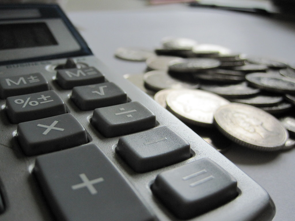 Calculadora e moedas sobre mesa, simbolizando cálculo de tributos